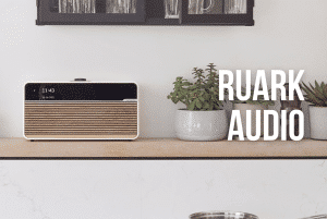 Ruark R1, Ruark R2, Ruark R3, Ruark 810 en Ruark 610 op een houten kast met een plantje er naast met de witte tekst 'Ruark Audio' erop voor een blog van Hifi Overgaauw leiden
